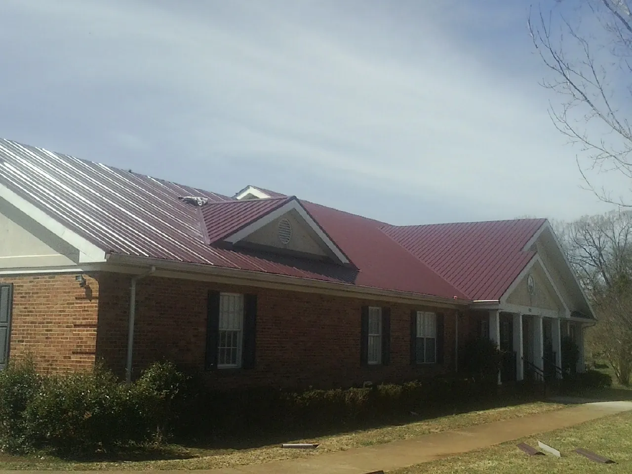 Red metal roof with gabled entries on a long brick building, from a Hail Damage Roof Repair job in Red Bluff