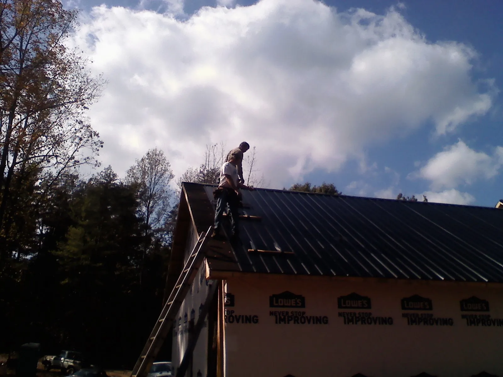 Roofer fastening dark metal panels high against a cloudy sky, from a Roof Inspection job in Red Bluff