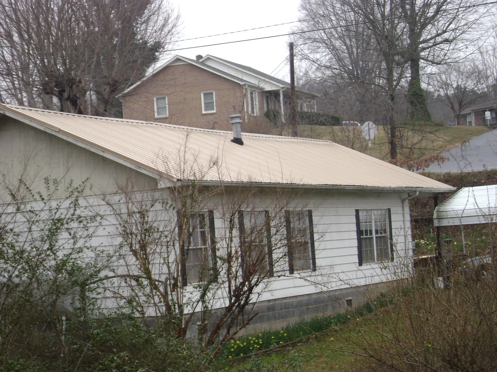 Tan metal roof on a white sided house set into a hillside — Commercial Roofing by Roofing Brothers in Red Bluff